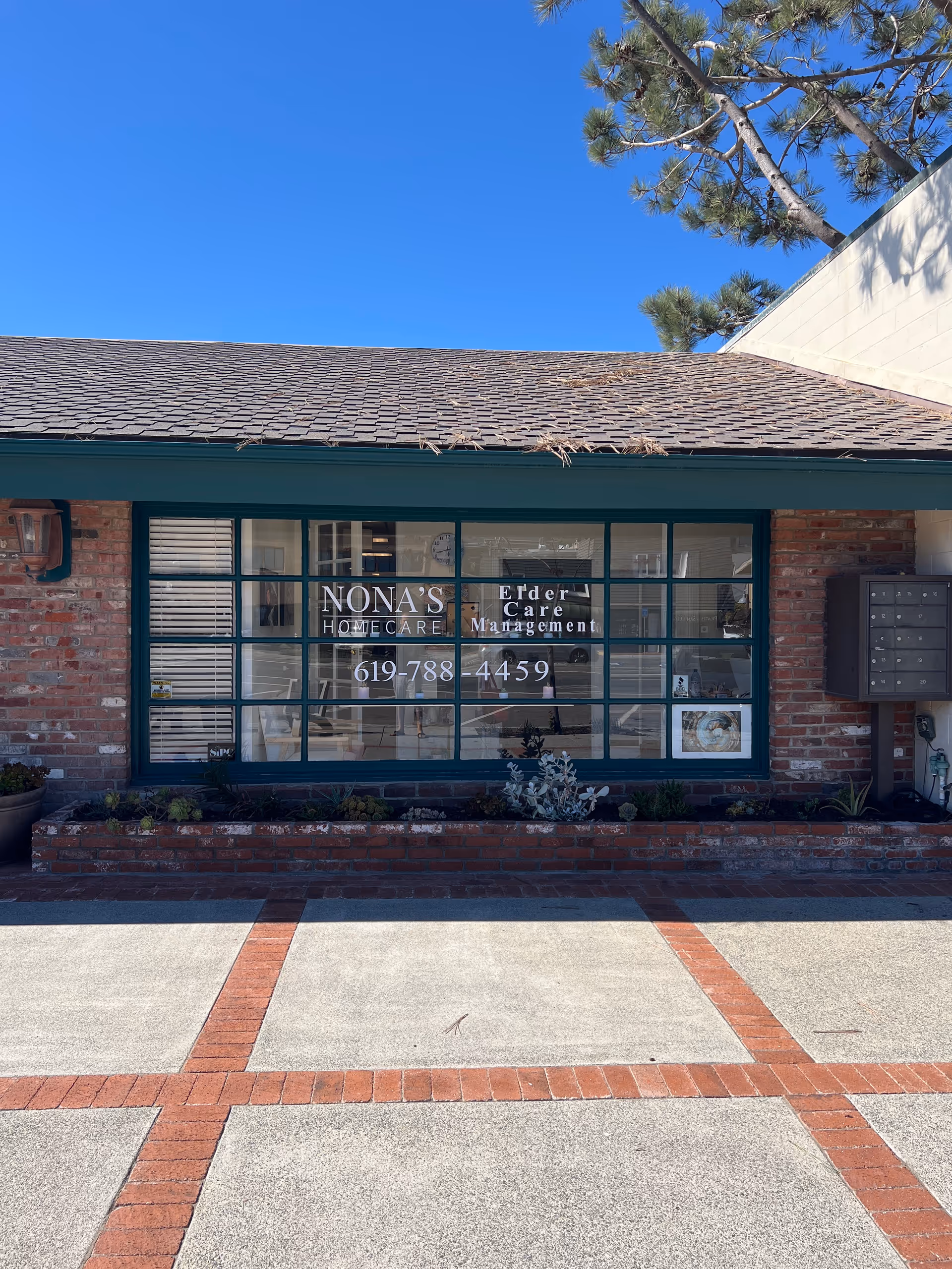 Brick storefront with large glass windows displaying Nona's Home Care sign.