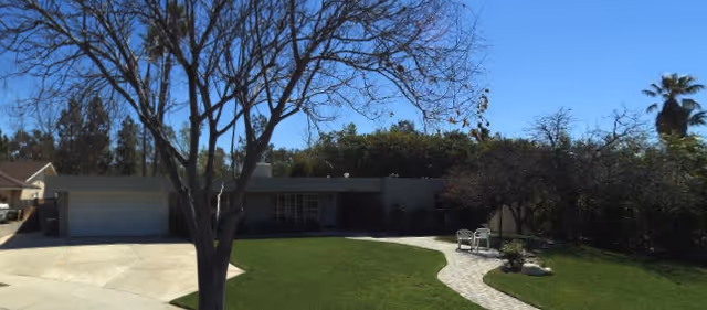 A single-story senior living home with a front yard, driveway, and leafless tree.