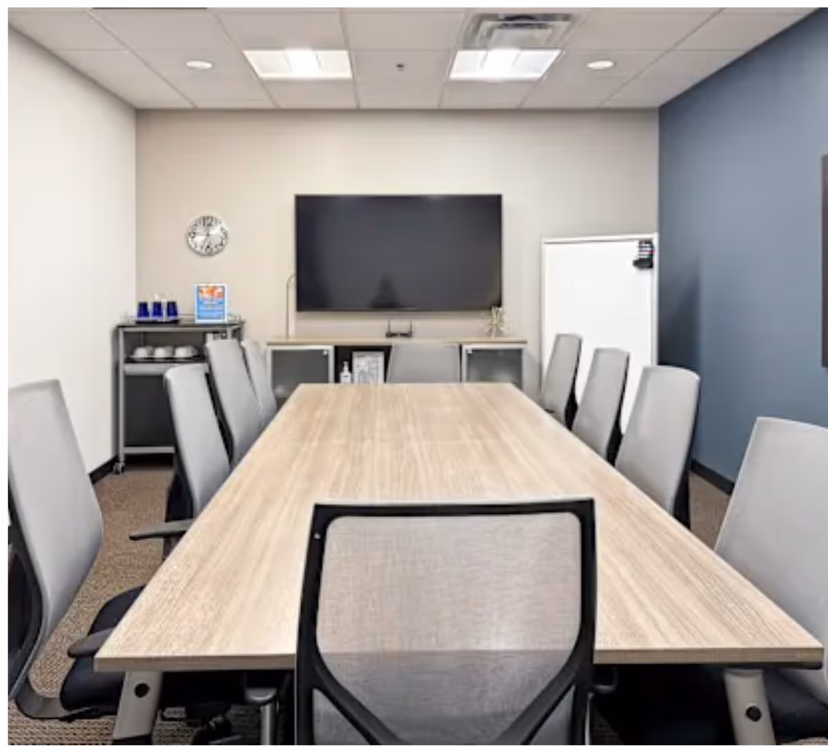 A long conference table with white chairs surrounds a central meeting room with a large screen.