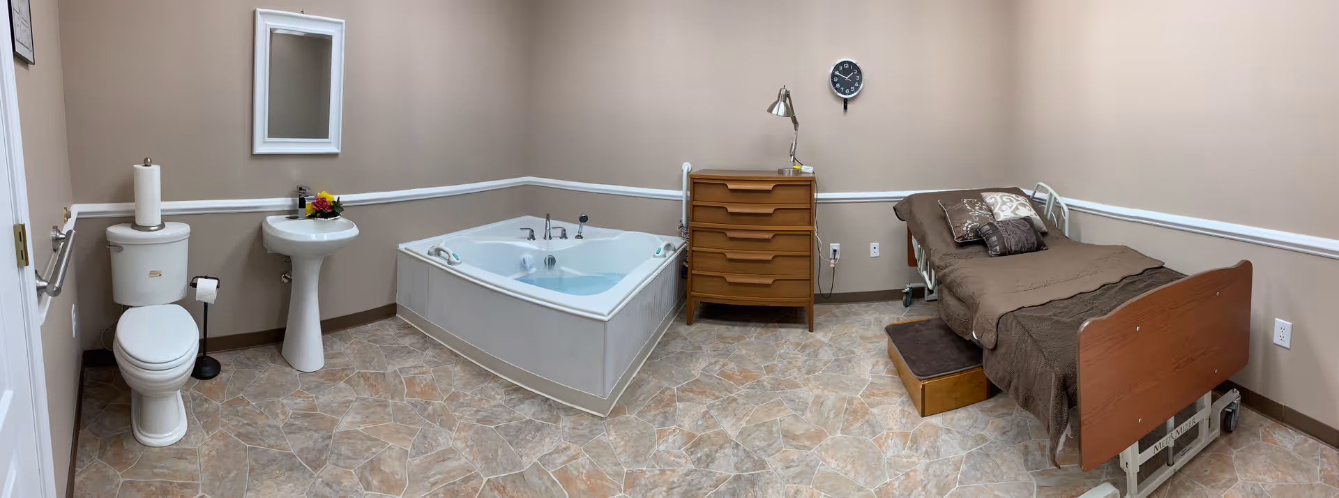 A senior living suite showing a toilet, sink, bathtub, dresser, and adjustable bed.