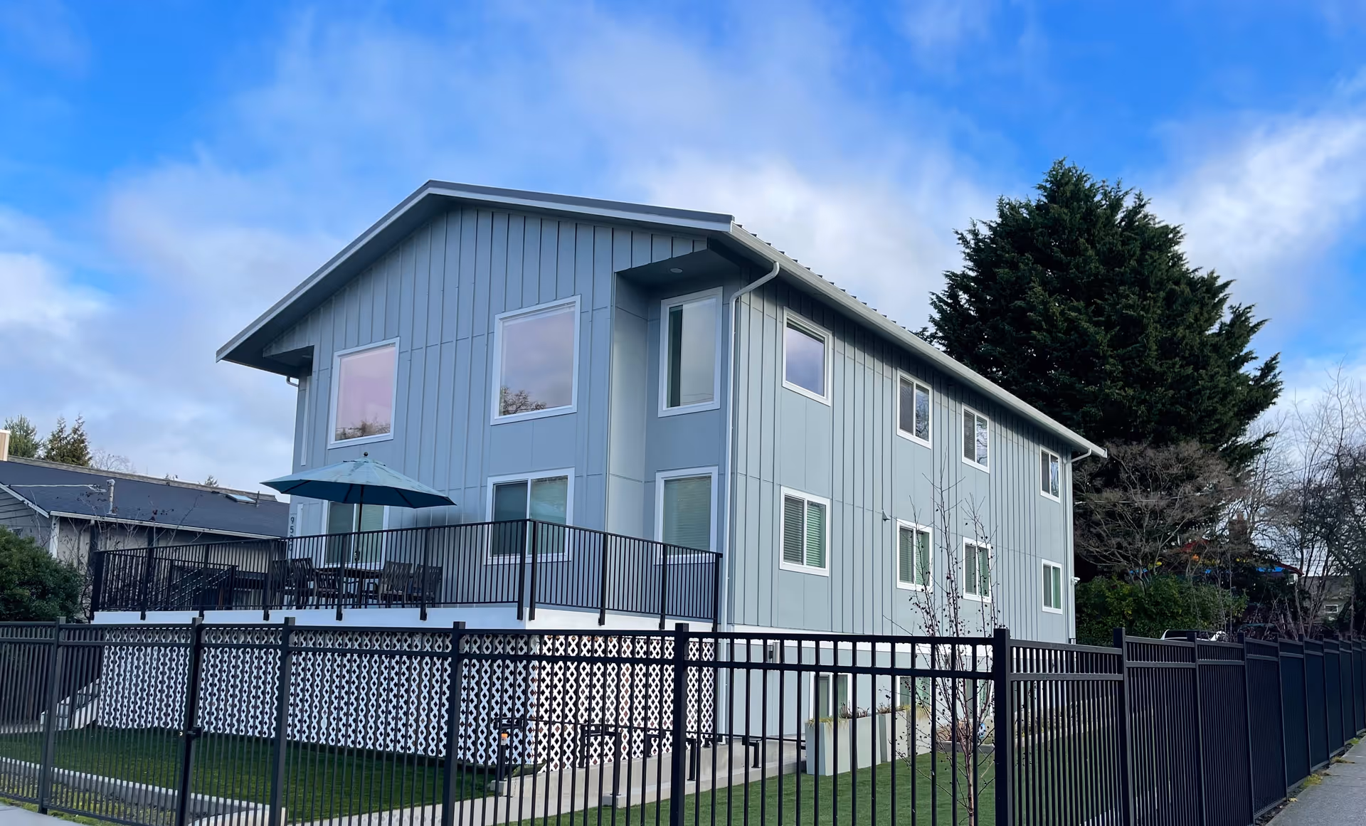 Two-story blue-gray senior living facility exterior with a fenced yard and outdoor deck.