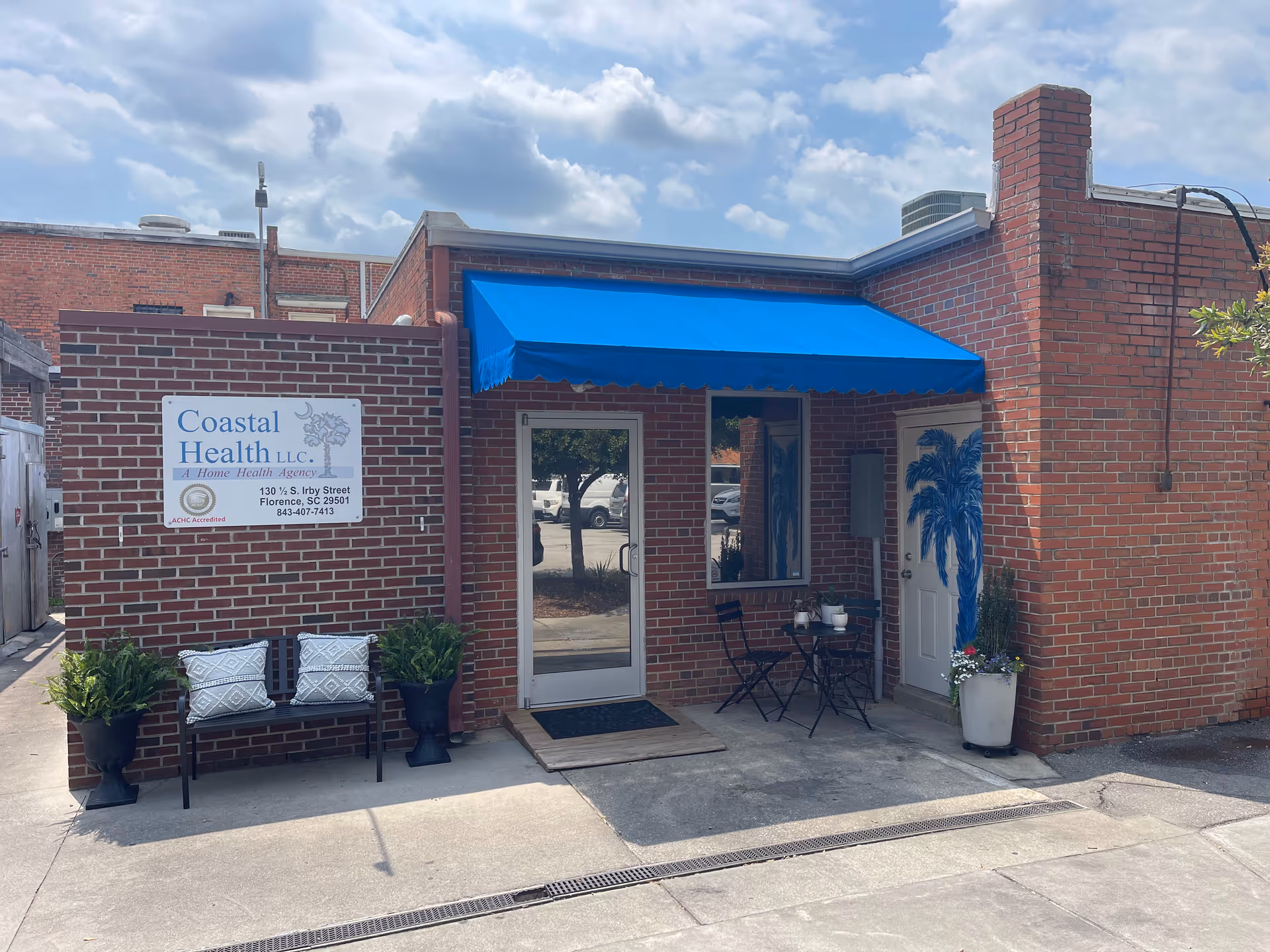 Brick building with Coastal Health, LLC sign, blue awning, and small outdoor seating area.