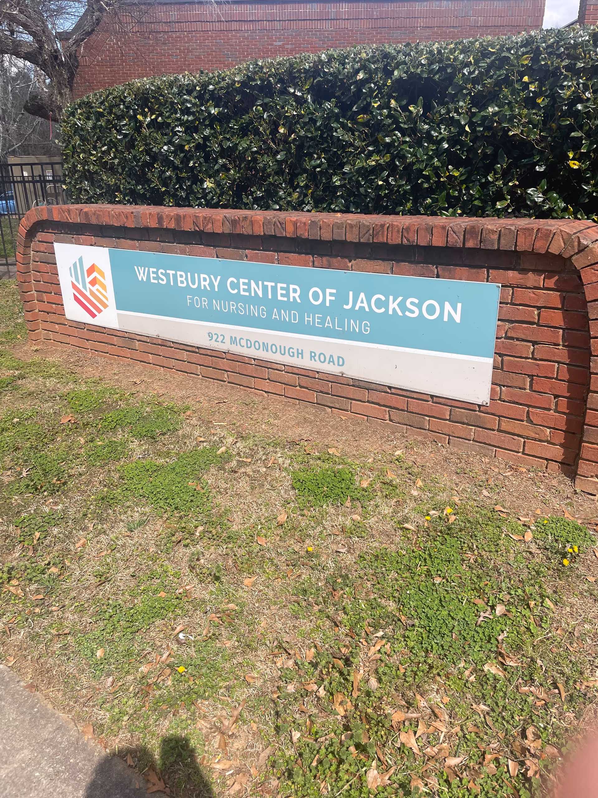 Brick sign for Westbury Center of Jackson for Nursing and Healing with hedges behind.