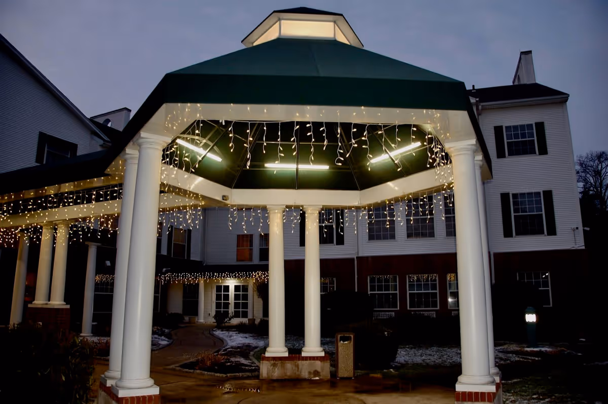Covered portico with white columns and hanging icicle string lights at the front entrance of a multi-story residential building at dusk.