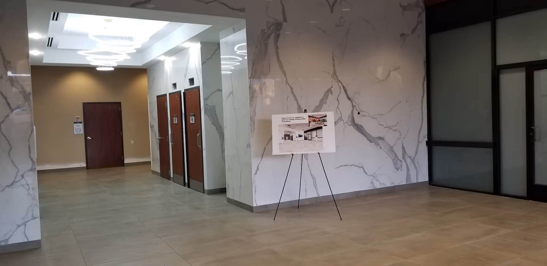 Lobby area with marble walls, elevators, and a display board on a tripod.