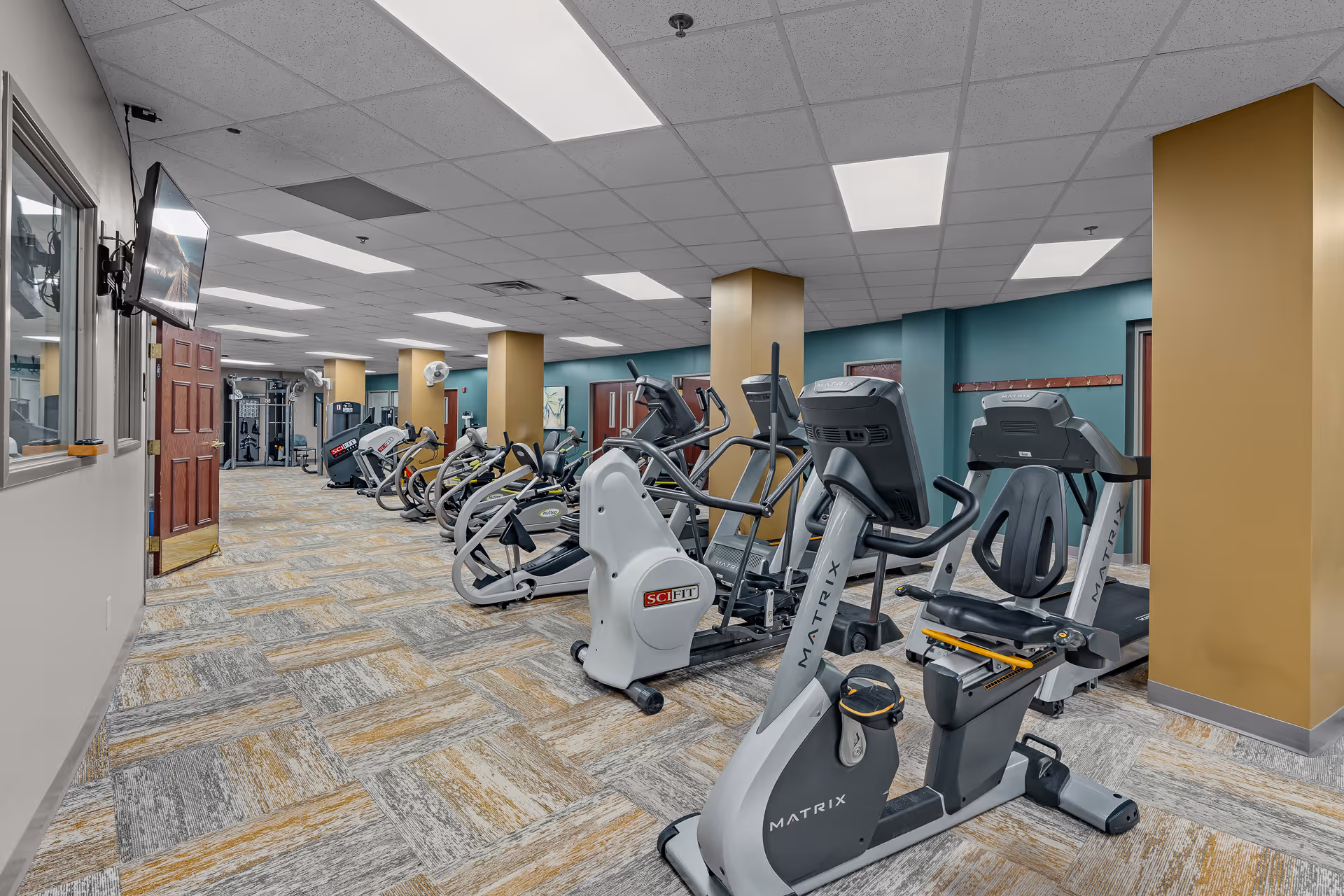 Interior fitness room with multiple cardio machines and exercise equipment arranged in rows.