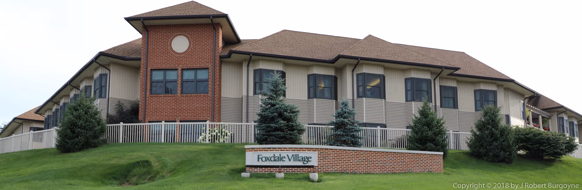 Exterior view of Foxdale Village senior living building with a brick sign and green lawn