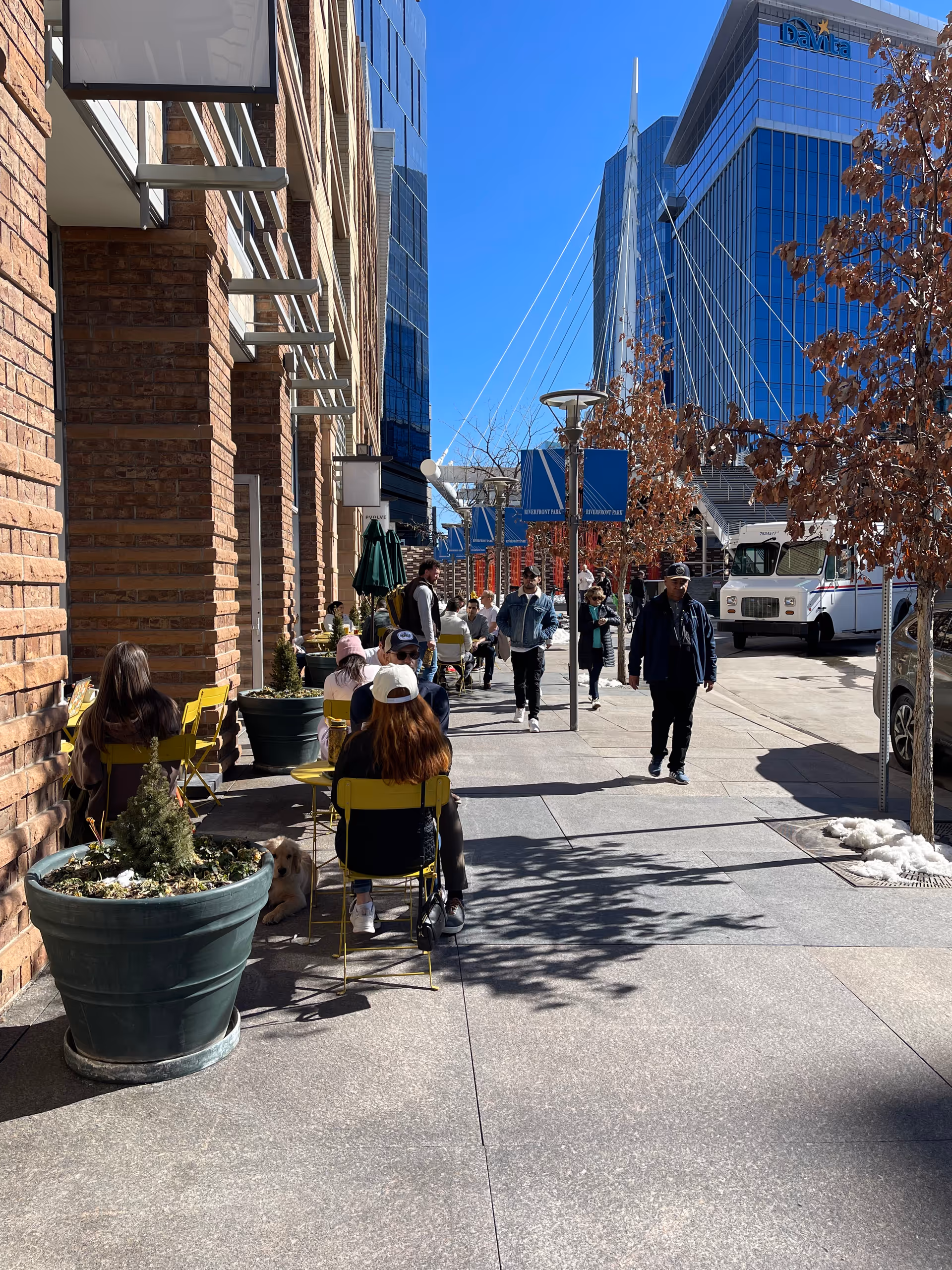 Outdoor sidewalk cafe with yellow chairs, pedestrians, and tall glass buildings.