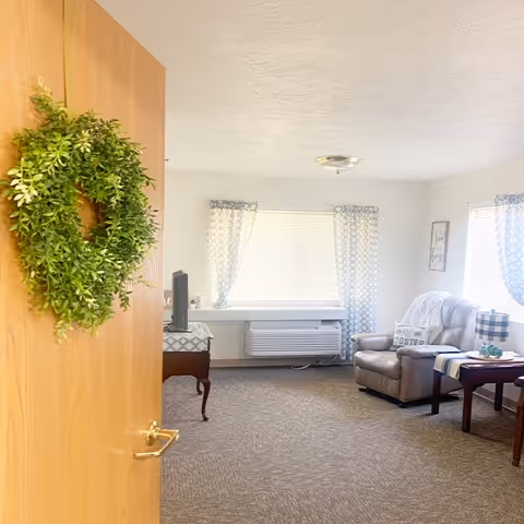 Open door reveals a cozy living room with sofa, coffee table, and wreath on door.