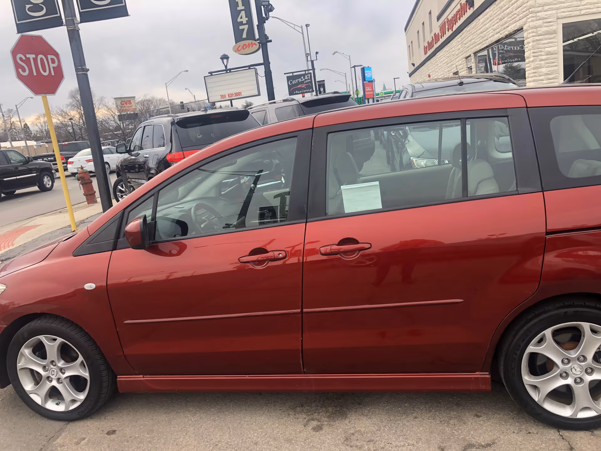 Red minivan parked on a city street beside a building with storefronts