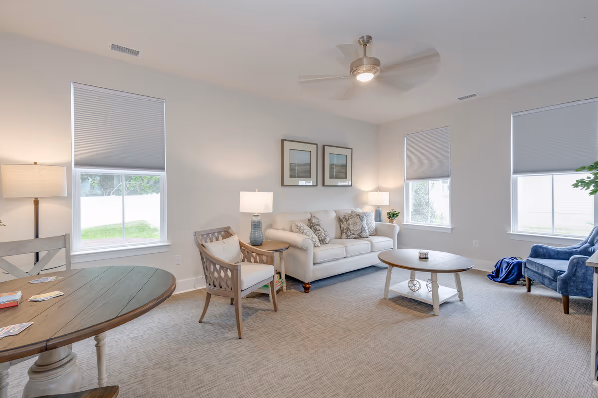 Bright living room with sofa, chairs, coffee table, lamps, and multiple windows.
