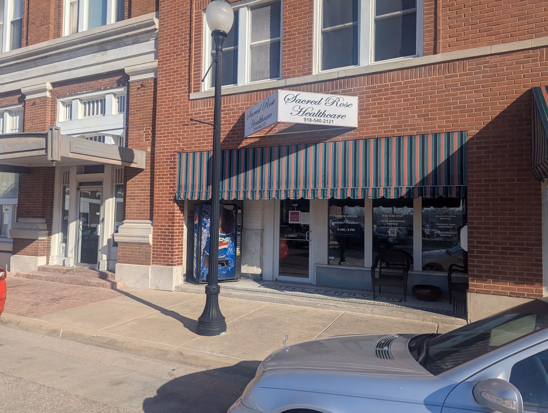 Brick storefront with striped awning and Sacred Rose Healthcare sign on a city street.