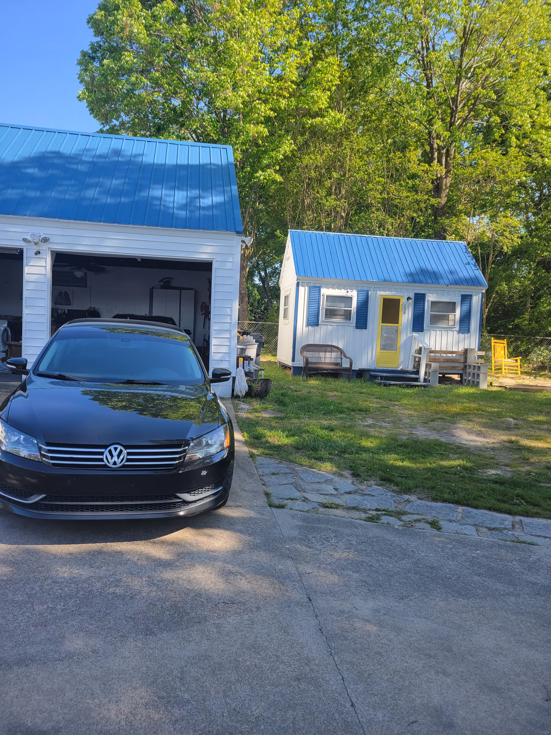 Blue-roofed houses and a black car parked on a driveway in a sunny yard.