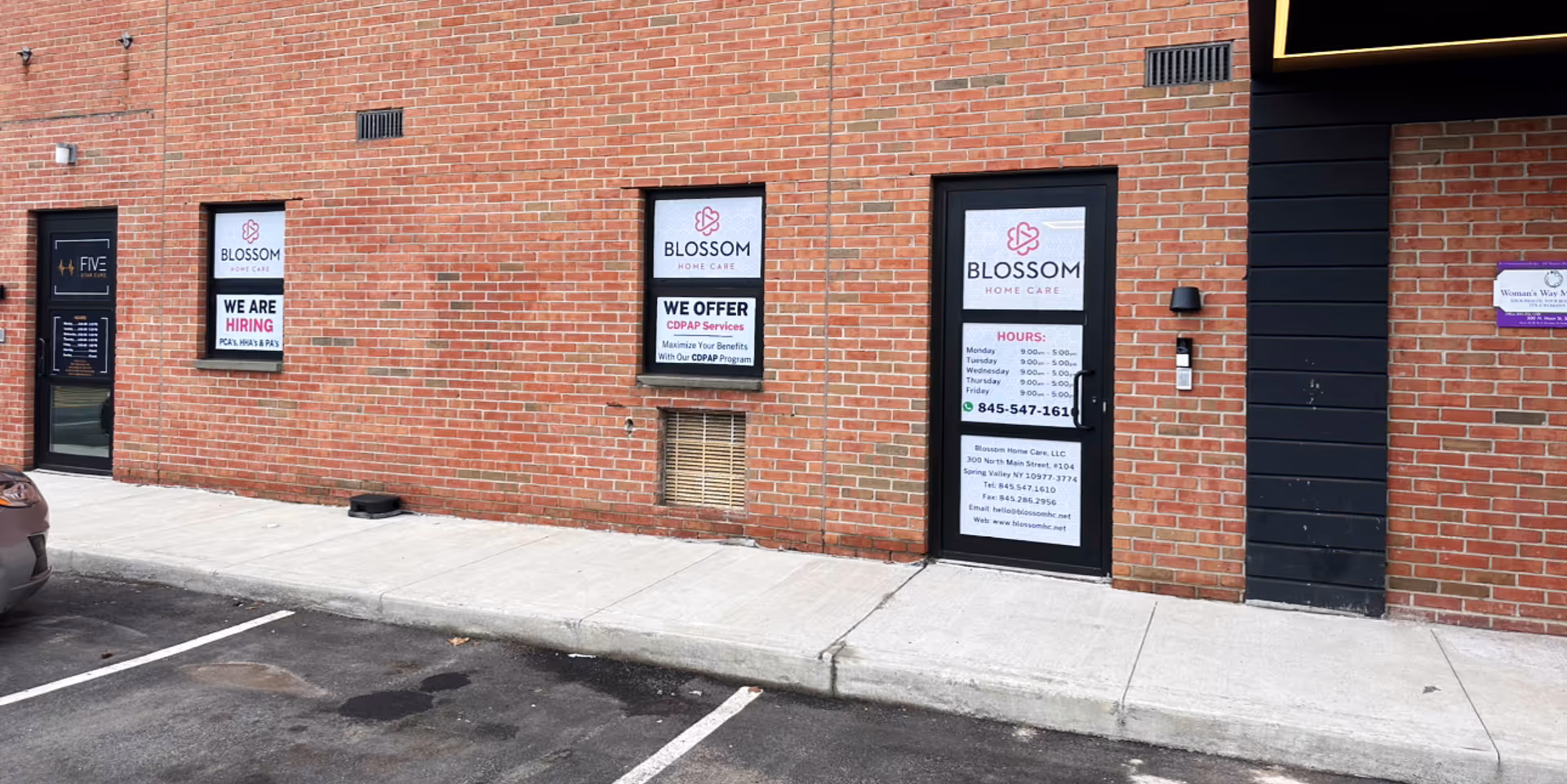 Exterior brick building with Blossom Home Care signs on doors along sidewalk.