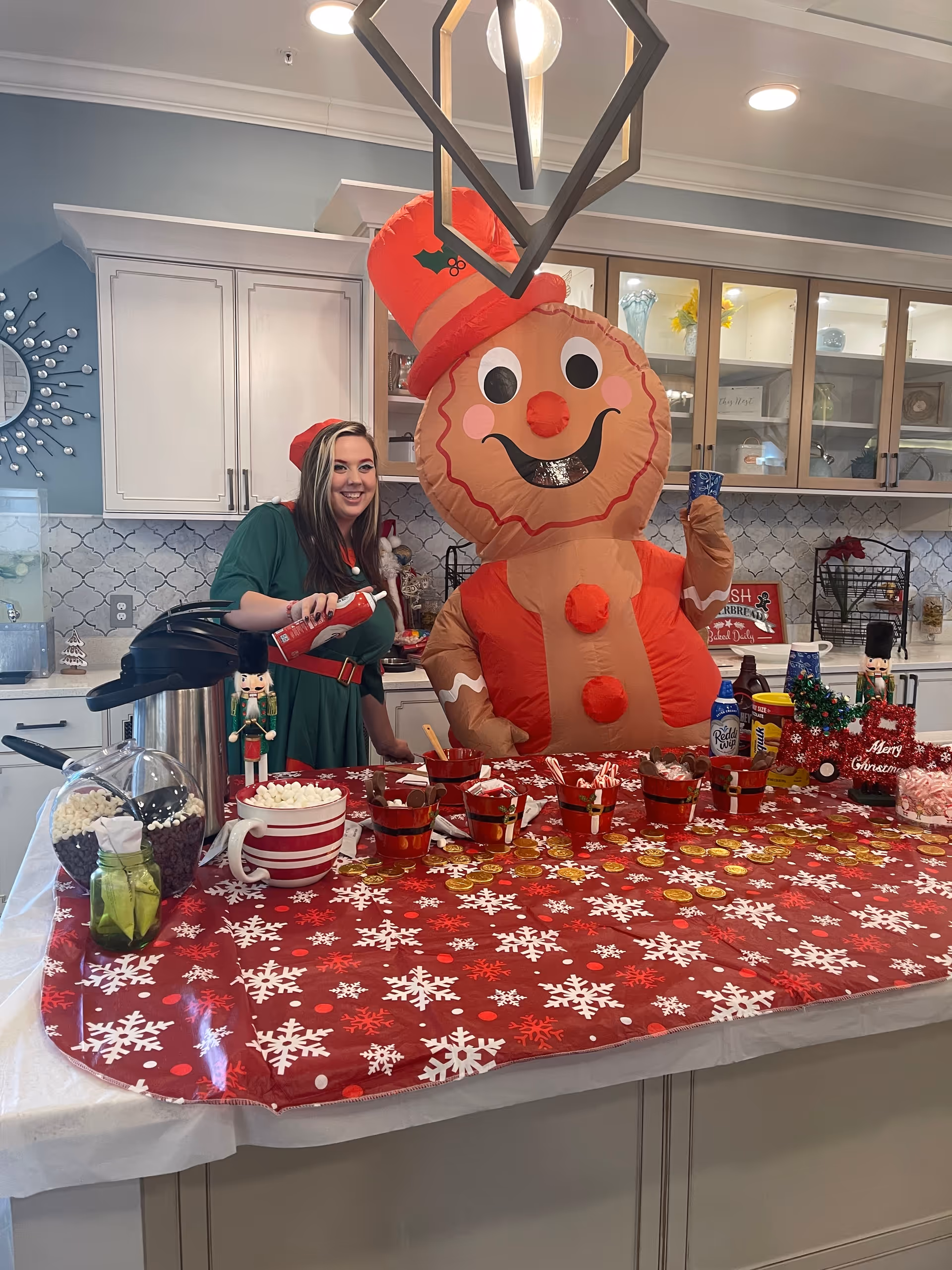 Staff member and oversized gingerbread figure decorate a festive kitchen counter.