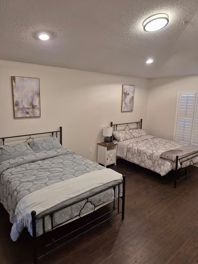 Two metal-framed beds with gray patterned bedding, nightstand, lamps, and wall art in a bedroom.