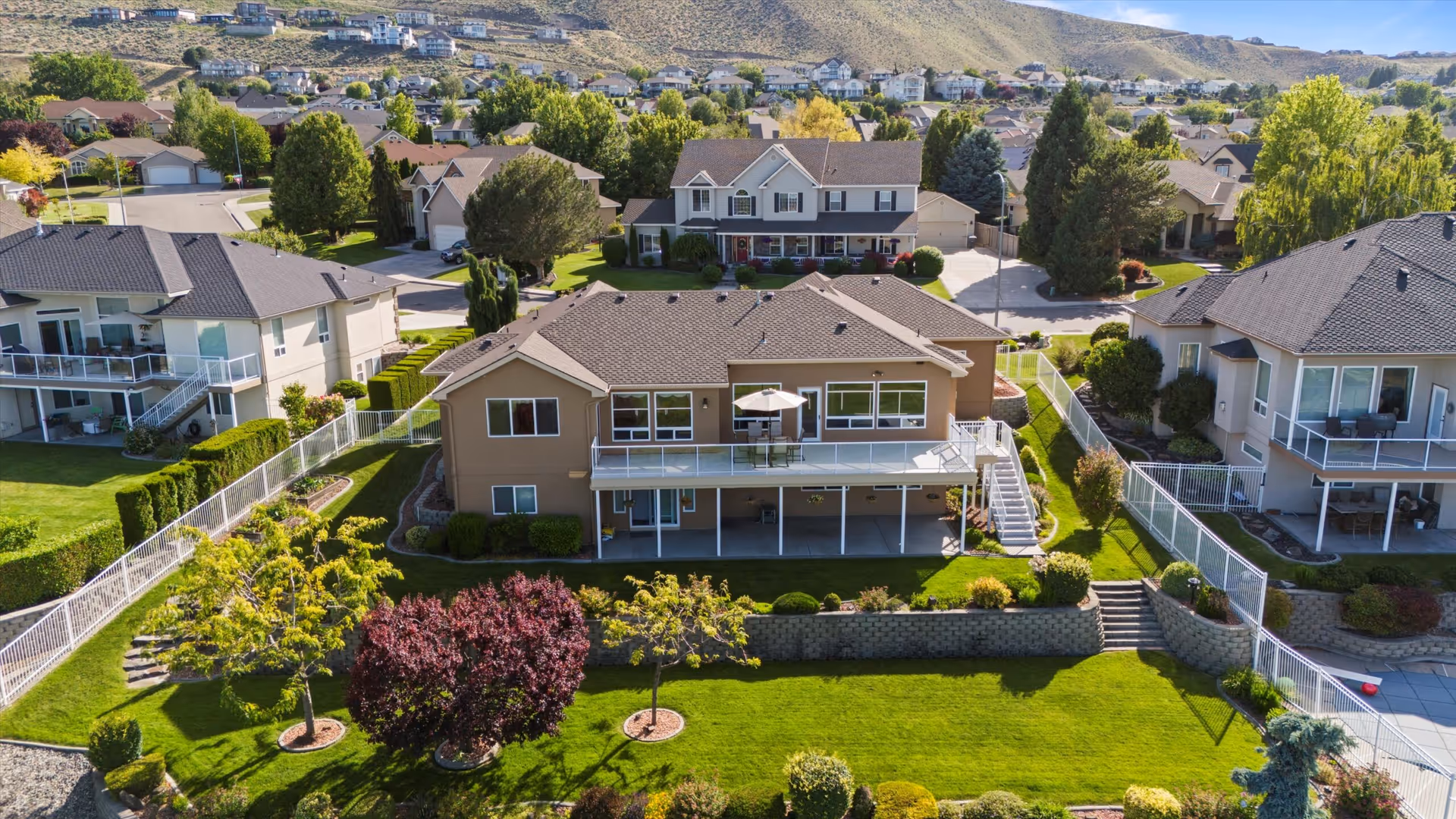 Aerial view of a two-story senior living home with a manicured lawn, large deck, and surrounding houses.
