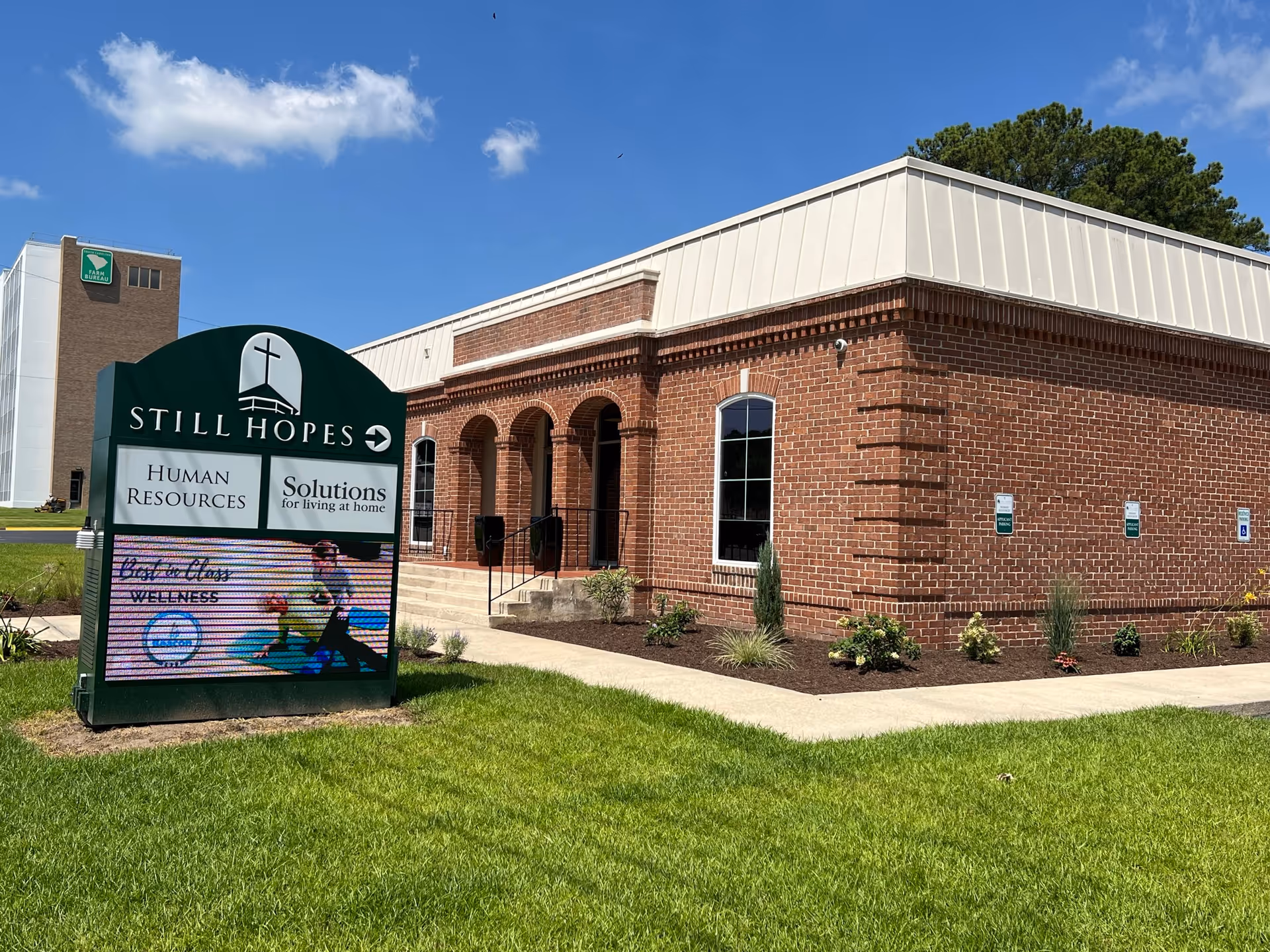 Brick senior-living facility with Still Hopes sign and landscaped front lawn.