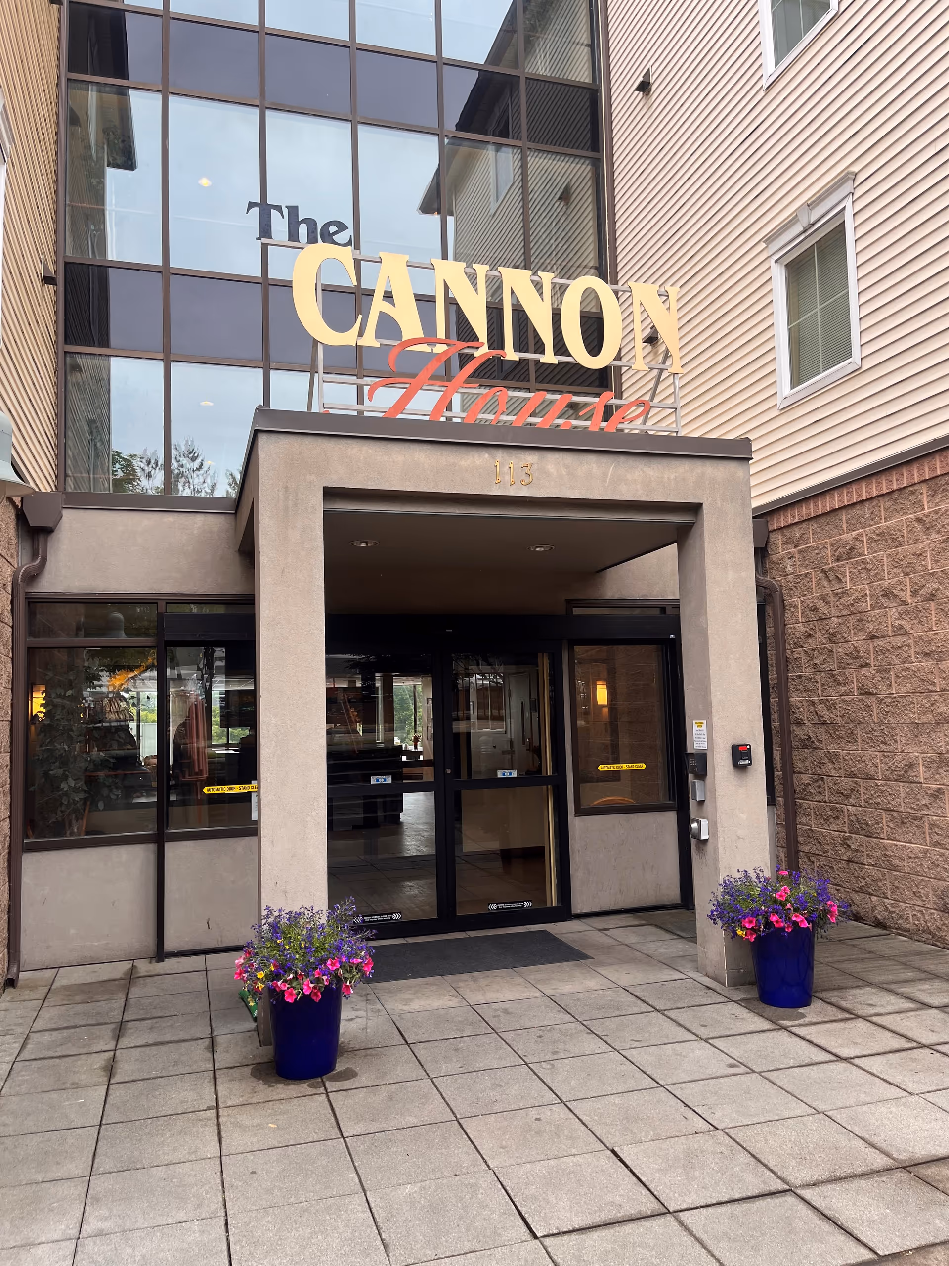 Exterior view of Sea Mar Cannon House entrance with glass doors and potted flowers.