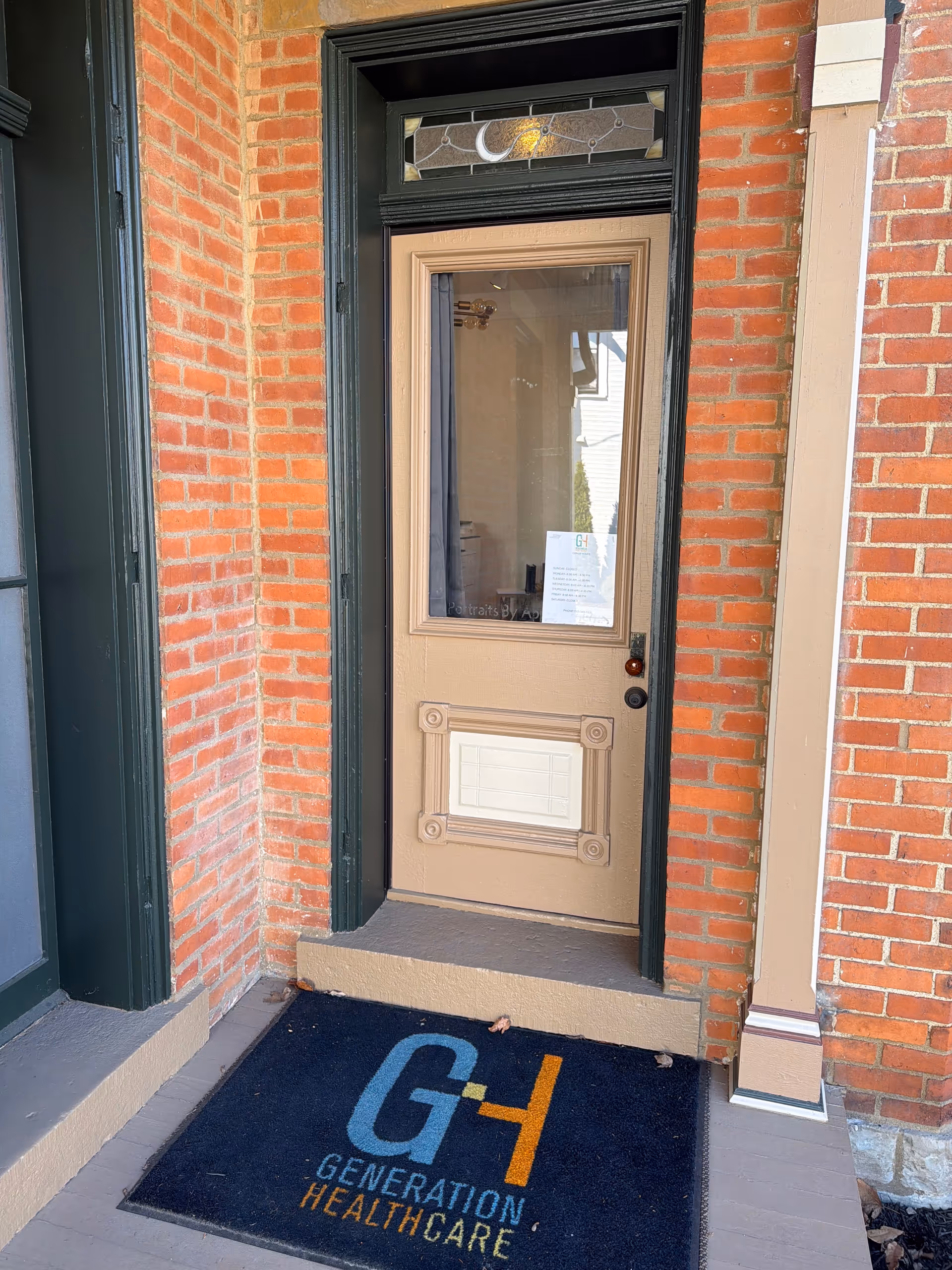 Brick front entrance with beige door and a Generation Healthcare mat outside.