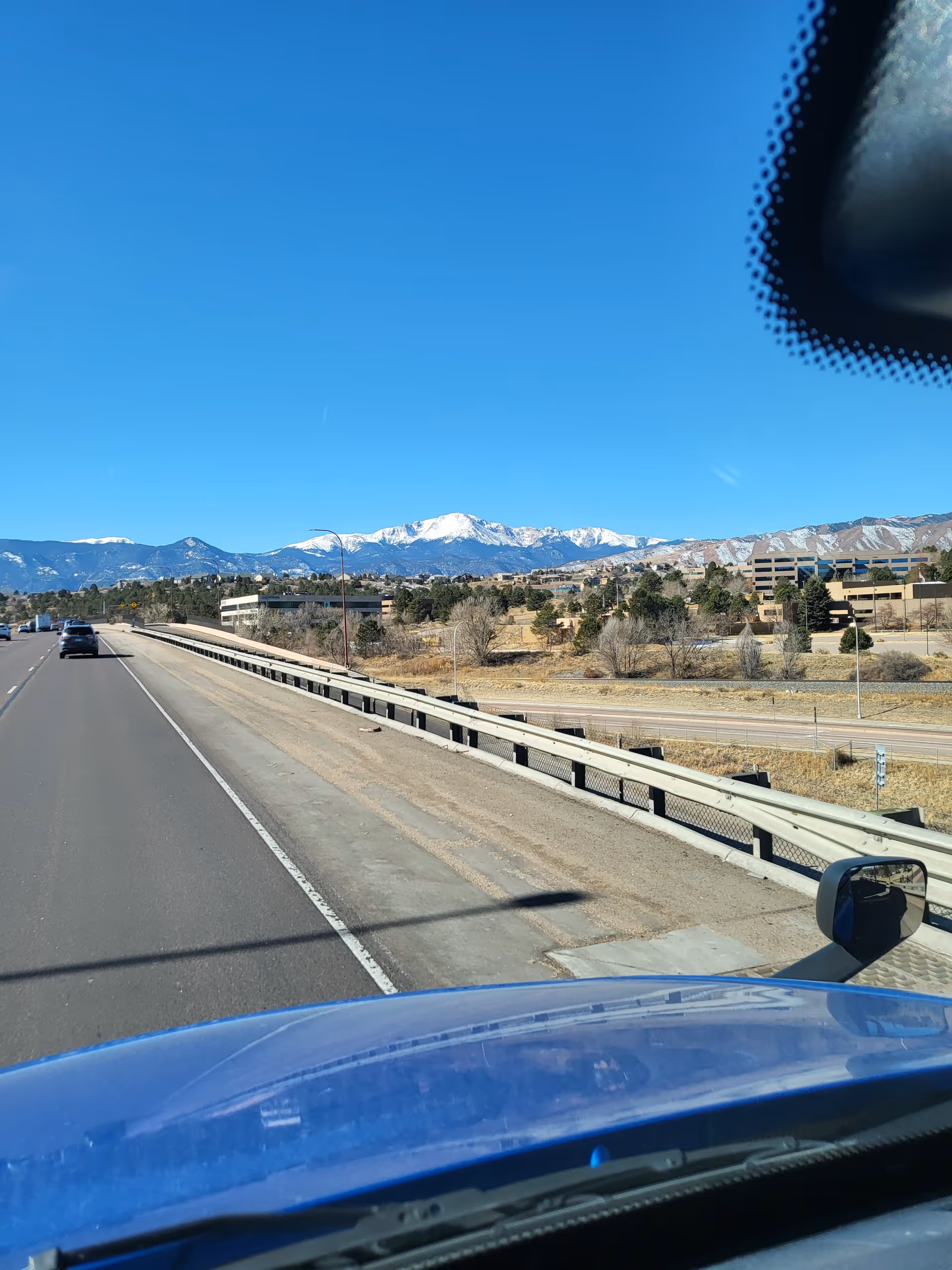 View from a vehicle shows a highway, mountains, and clear blue sky.