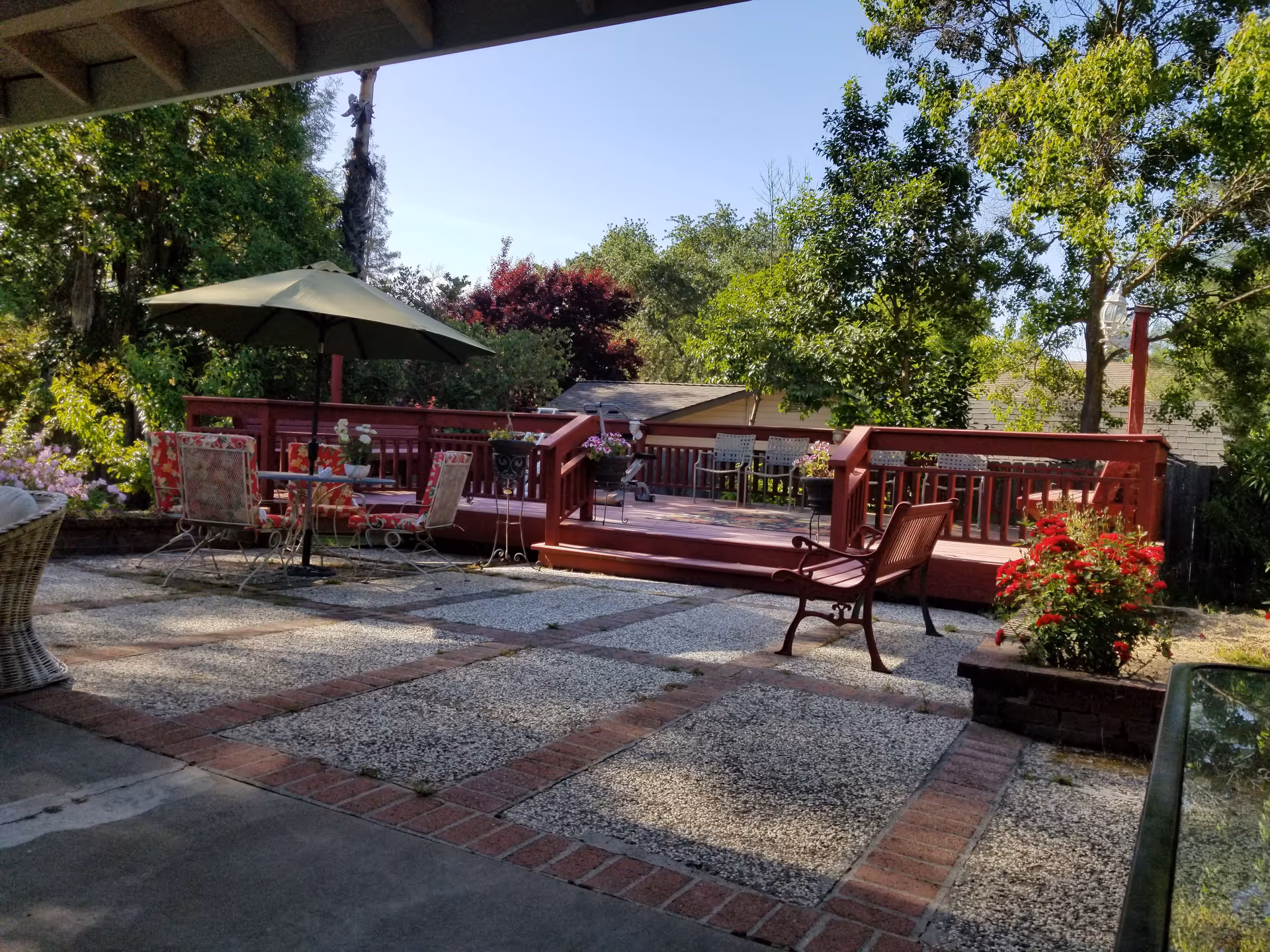 Sunny outdoor patio with red wooden deck, chairs, umbrella, and potted plants.