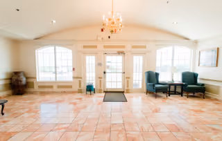 Bright lobby entrance with tiled floor, chandeliers, and blue seating in a senior living center.