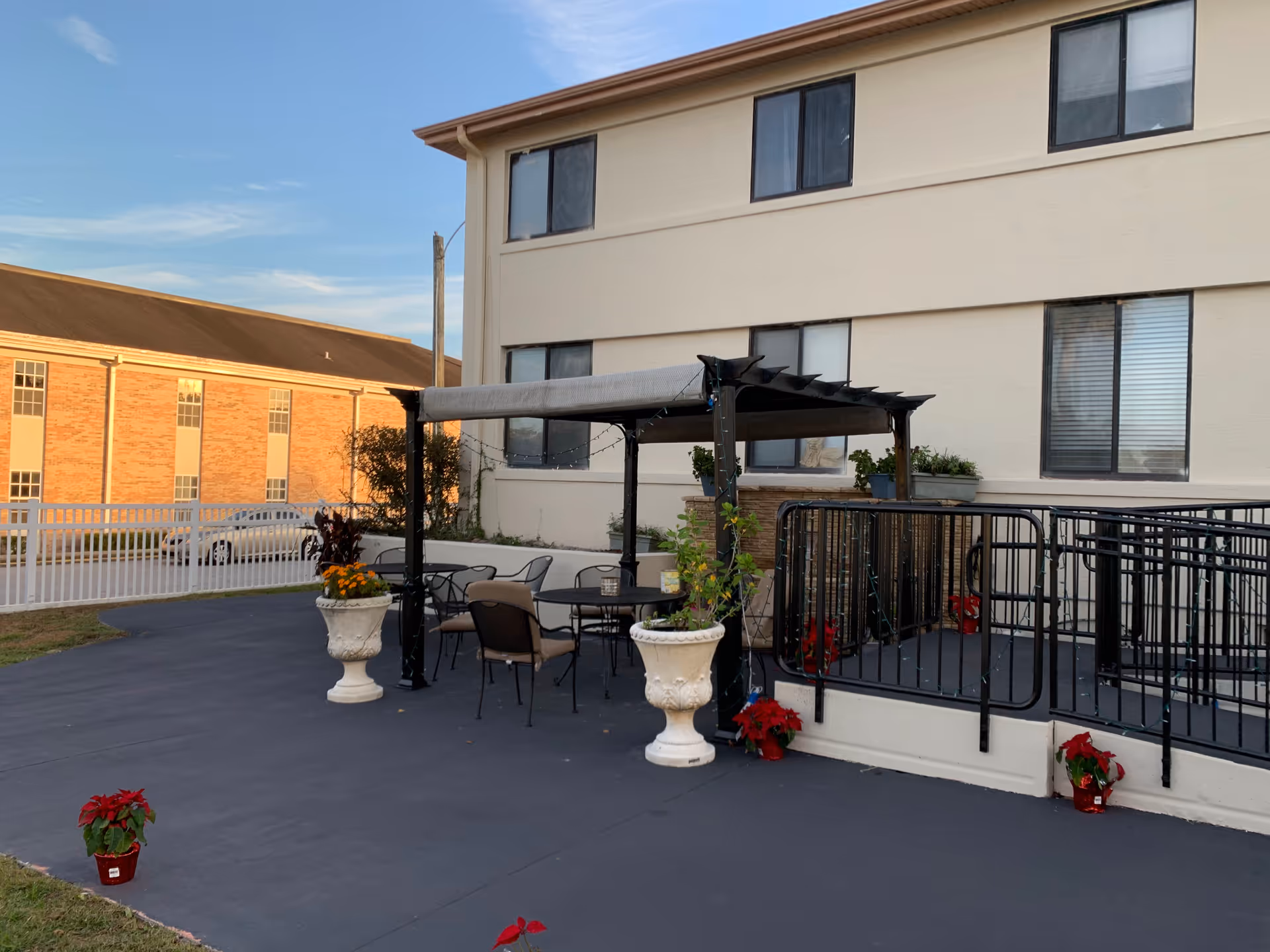 Outdoor patio with a pergola, table and chairs, and potted plants near a beige building.