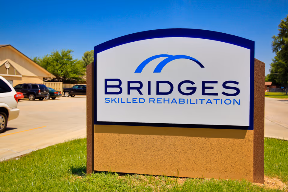 Exterior sign for Bridges Skilled Rehabilitation at a facility entrance with parked cars.