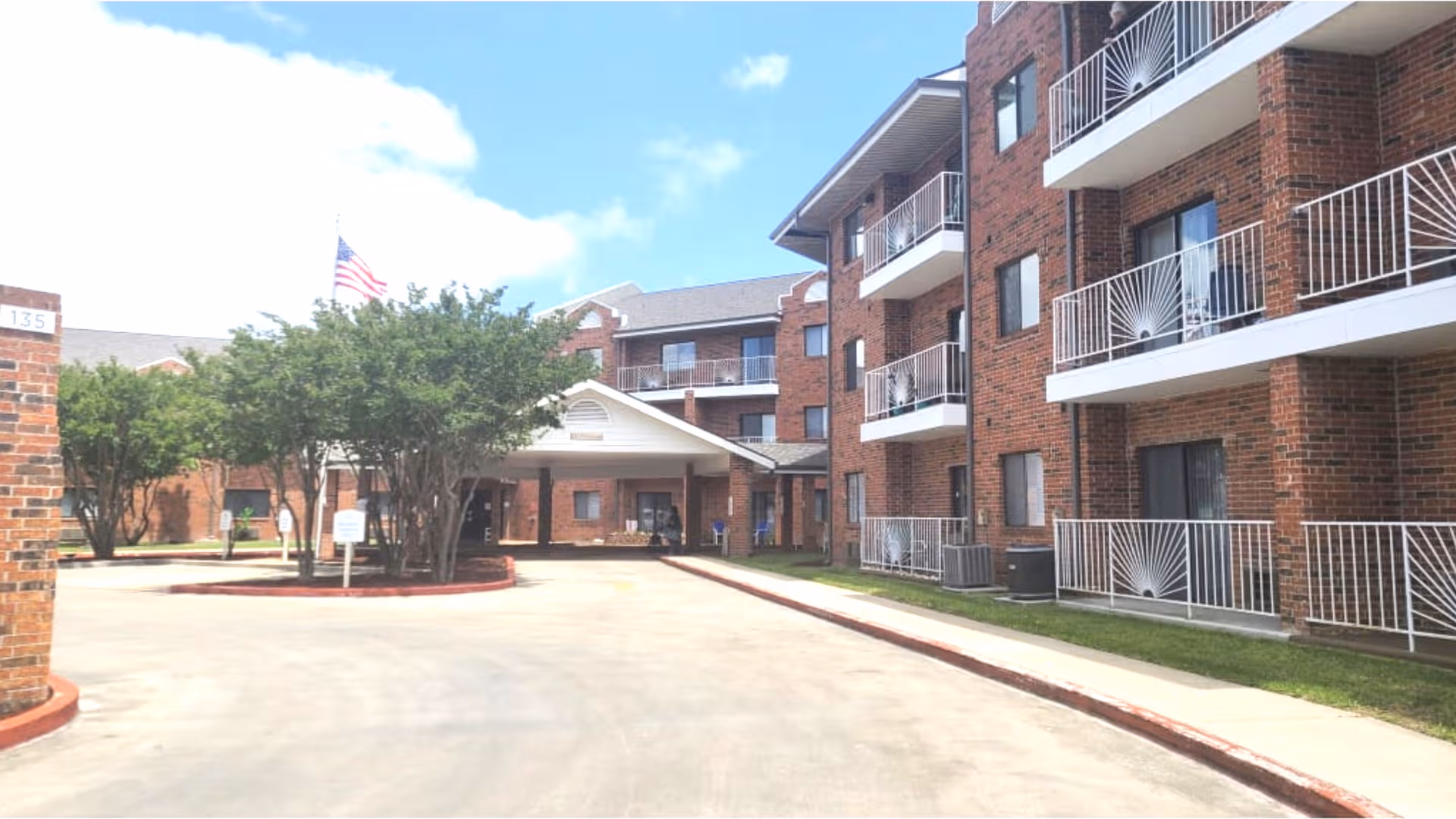 Brick senior living building with balconies along a curved driveway and front entrance canopy.