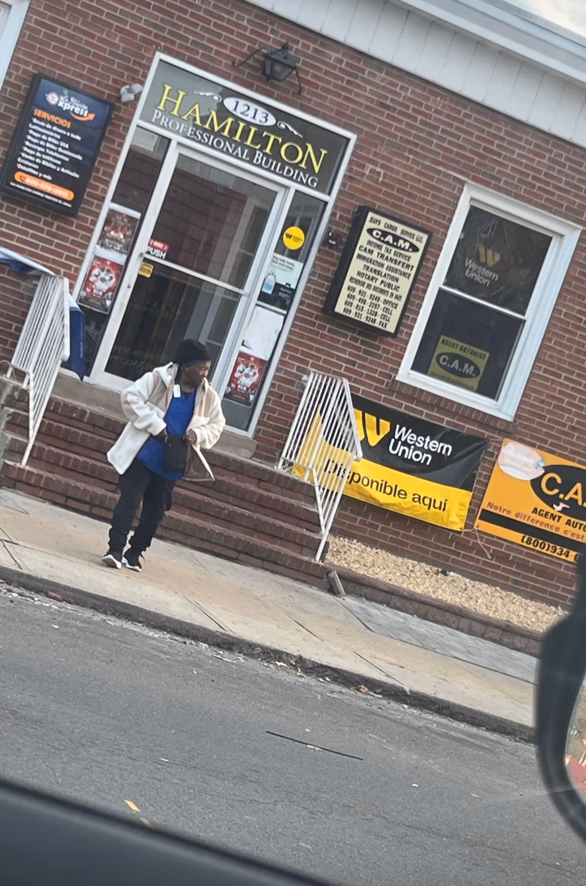 A person walks down steps outside a brick building with storefront signs.