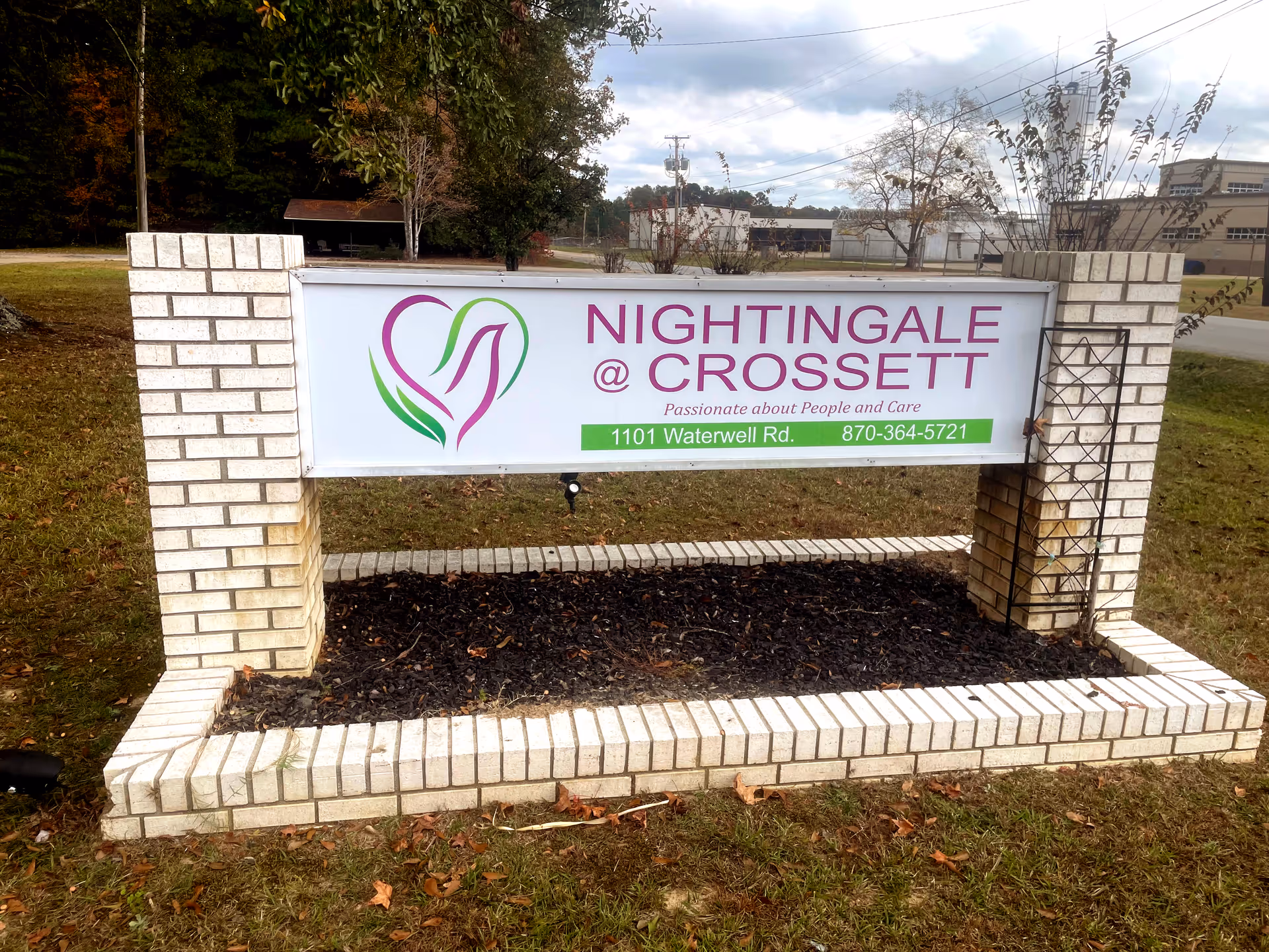 Brick-framed outdoor sign for Nightingale at Crossett with lawn and trees