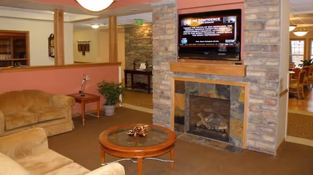 Cozy common living area with a stone fireplace, mounted TV, sofas, and a round coffee table.
