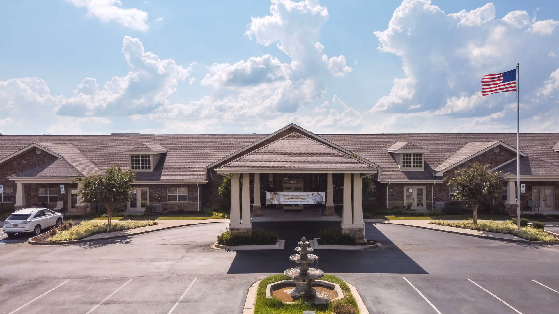 Exterior view of Hearthside Senior Living front entrance with fountain, flag, and driveway.