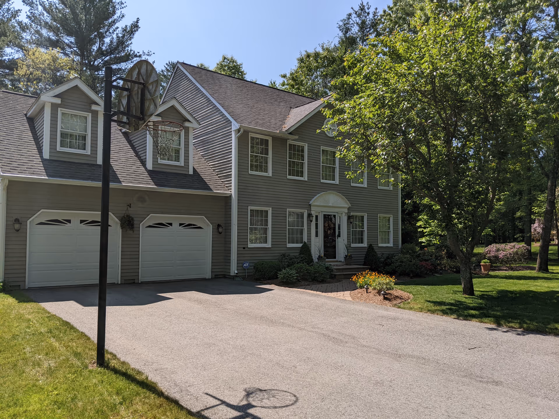 Two-story gray house with a front porch, two-car garage, and landscaped yard.