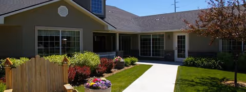 Single-story assisted living building with front entrance, walkway, and manicured landscaping.