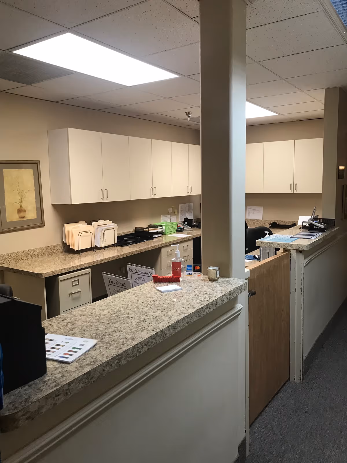 Reception desk with granite countertop and white cabinets in a facility hallway.