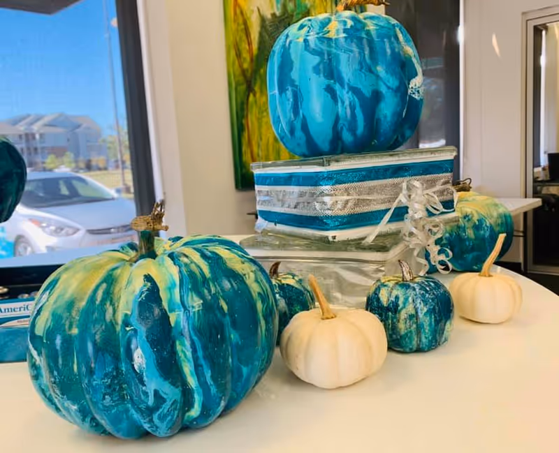 Blue-green pumpkins and a decorative gift stack adorn a table inside a senior living facility.