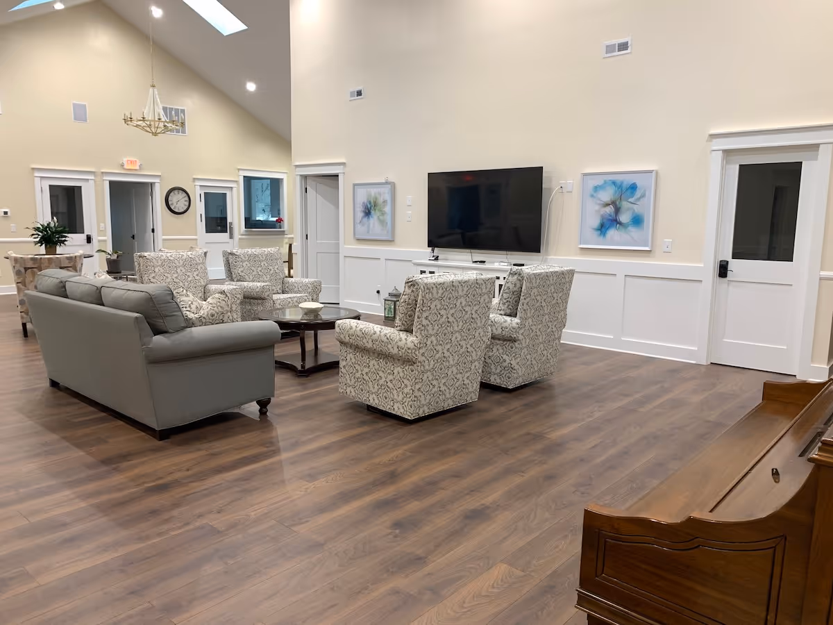 A spacious senior living common room with sofas, armchairs, a coffee table, TV, and artwork.