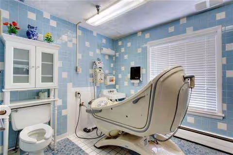 Hospital-style bath chair in a tiled, accessible bathroom at a facility.