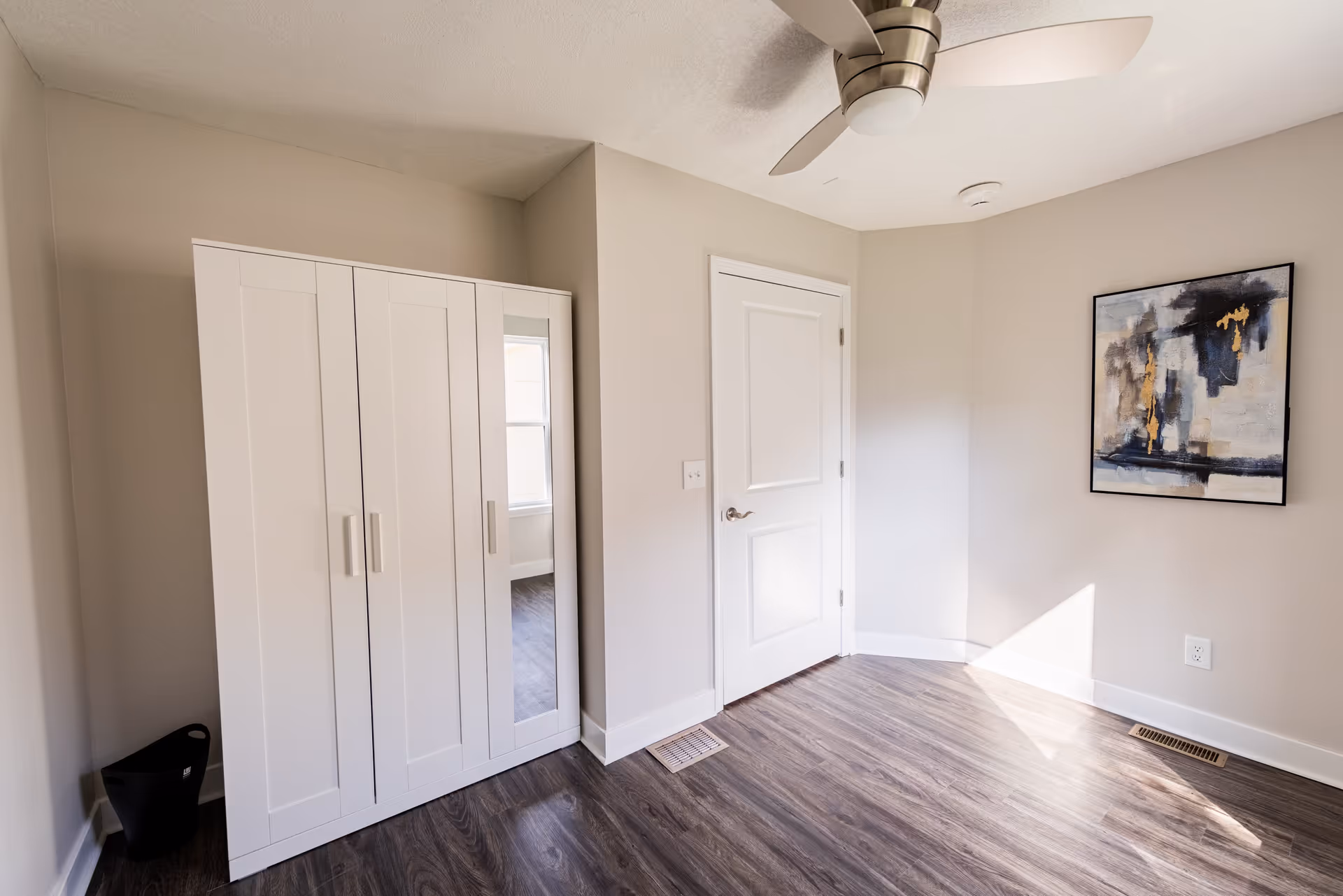 Empty bedroom with white closet, door, wall art, ceiling fan, and wood laminate flooring.