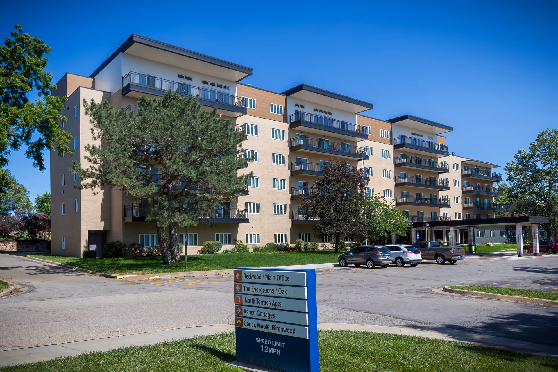 Exterior of Brewster Place senior living building with balconies, trees, and cars.