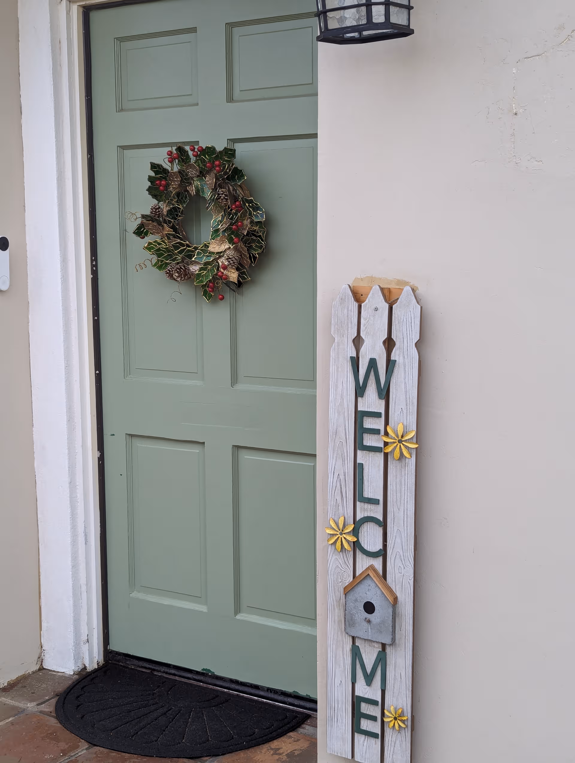 Green front door with a wreath and a vertical 'Welcome Home' sign beside it.