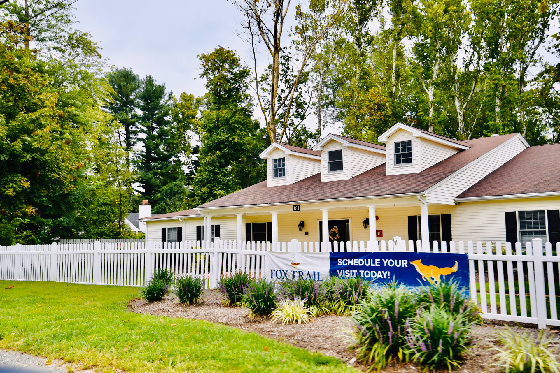 Front view of Fox Trail Memory Care Living with white picket fence and banner.
