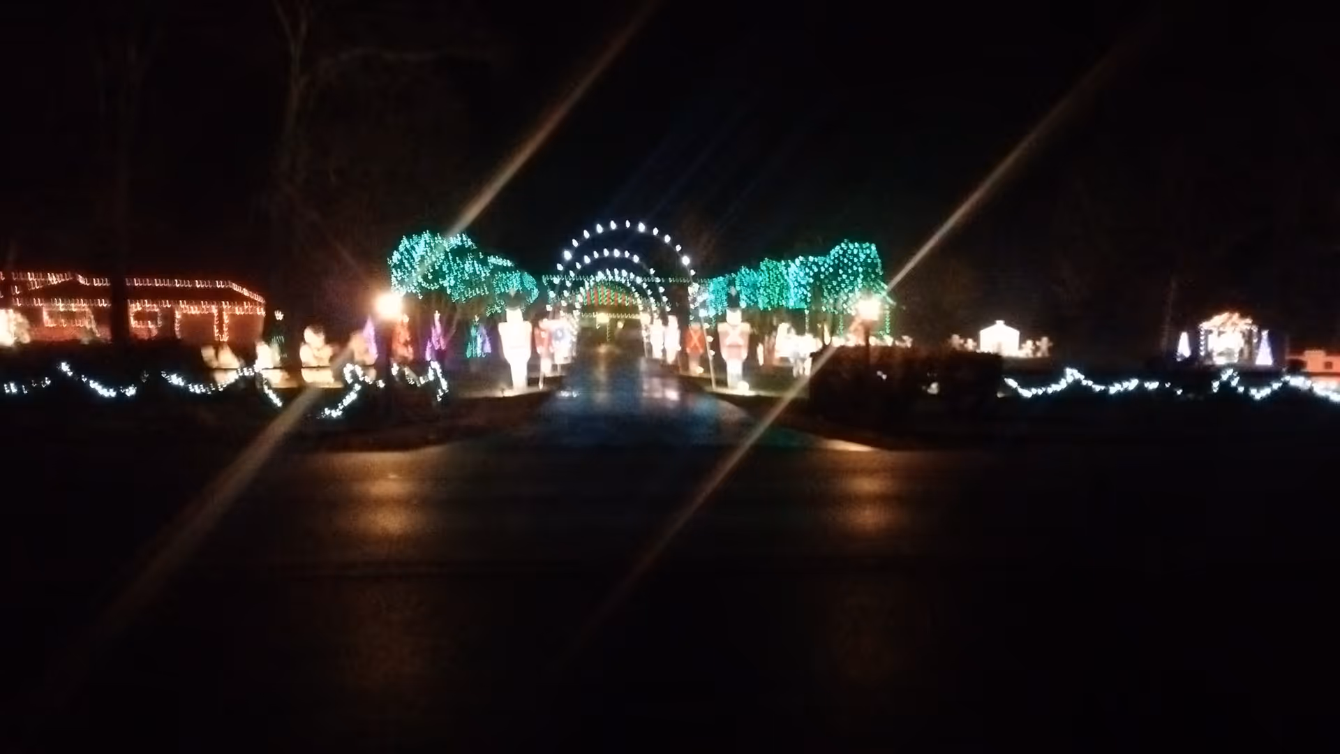 Night view of a lit walkway with colorful holiday arches and trees at Sagepoint Memory Care