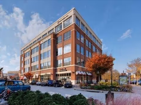 A multi-story brick senior living building with a parking lot and blue sky.