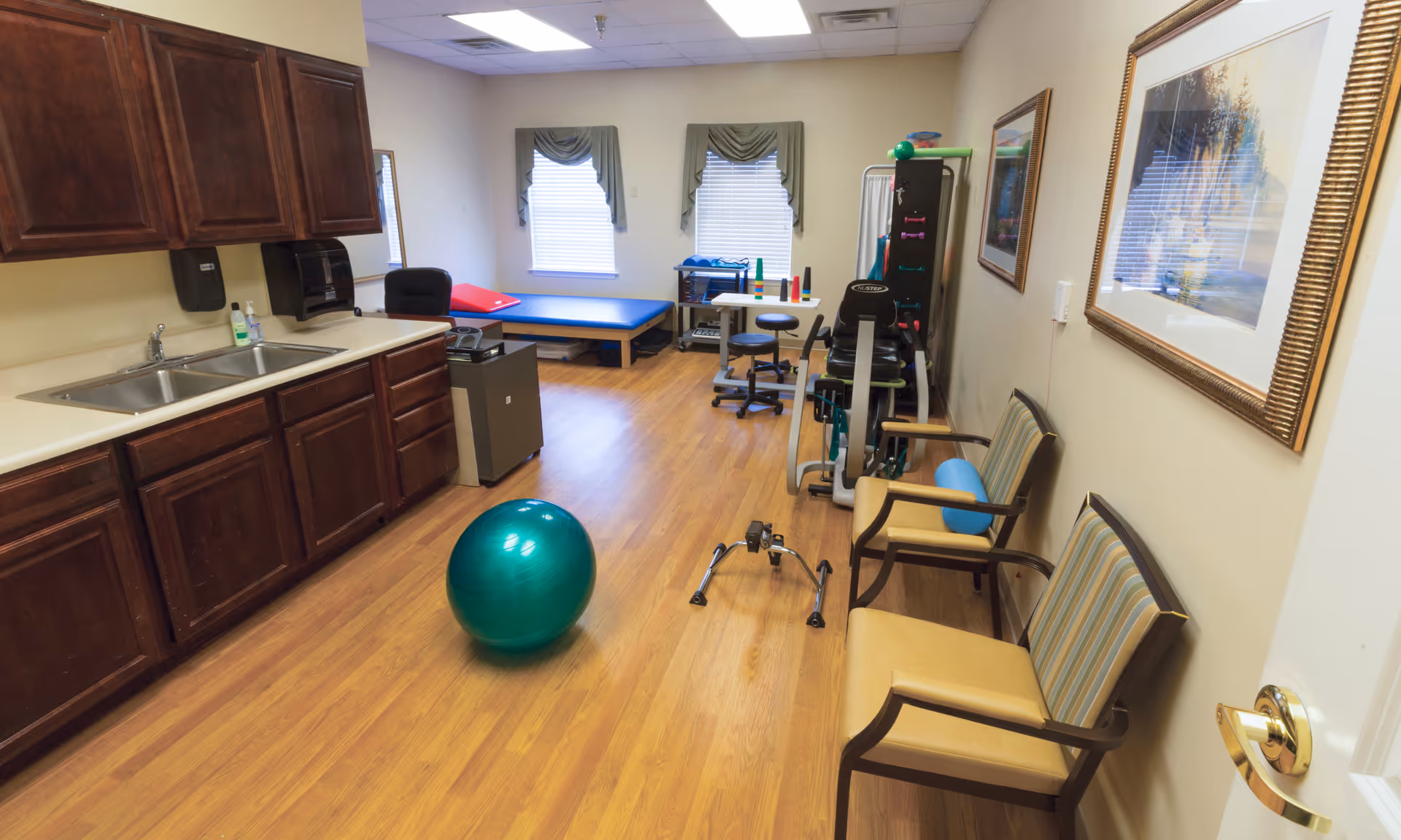 Interior with dark wood cabinets, sink, exercise equipment, a green exercise ball, and chairs.