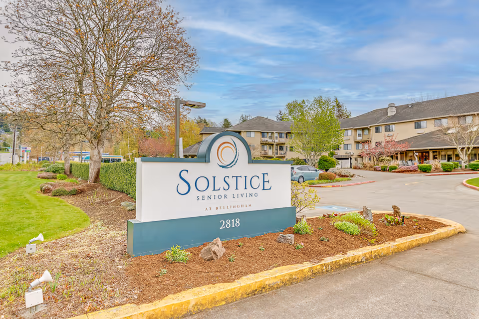 Exterior view of Solstice Senior Living at Bellingham sign with landscaped entry and building in background.