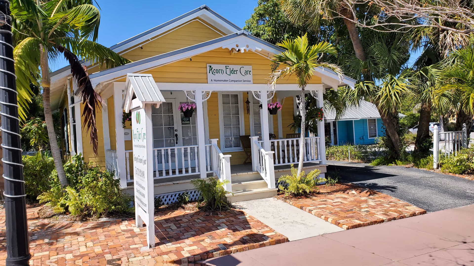 Yellow Acorn Elder Care building with a white porch and hanging baskets.