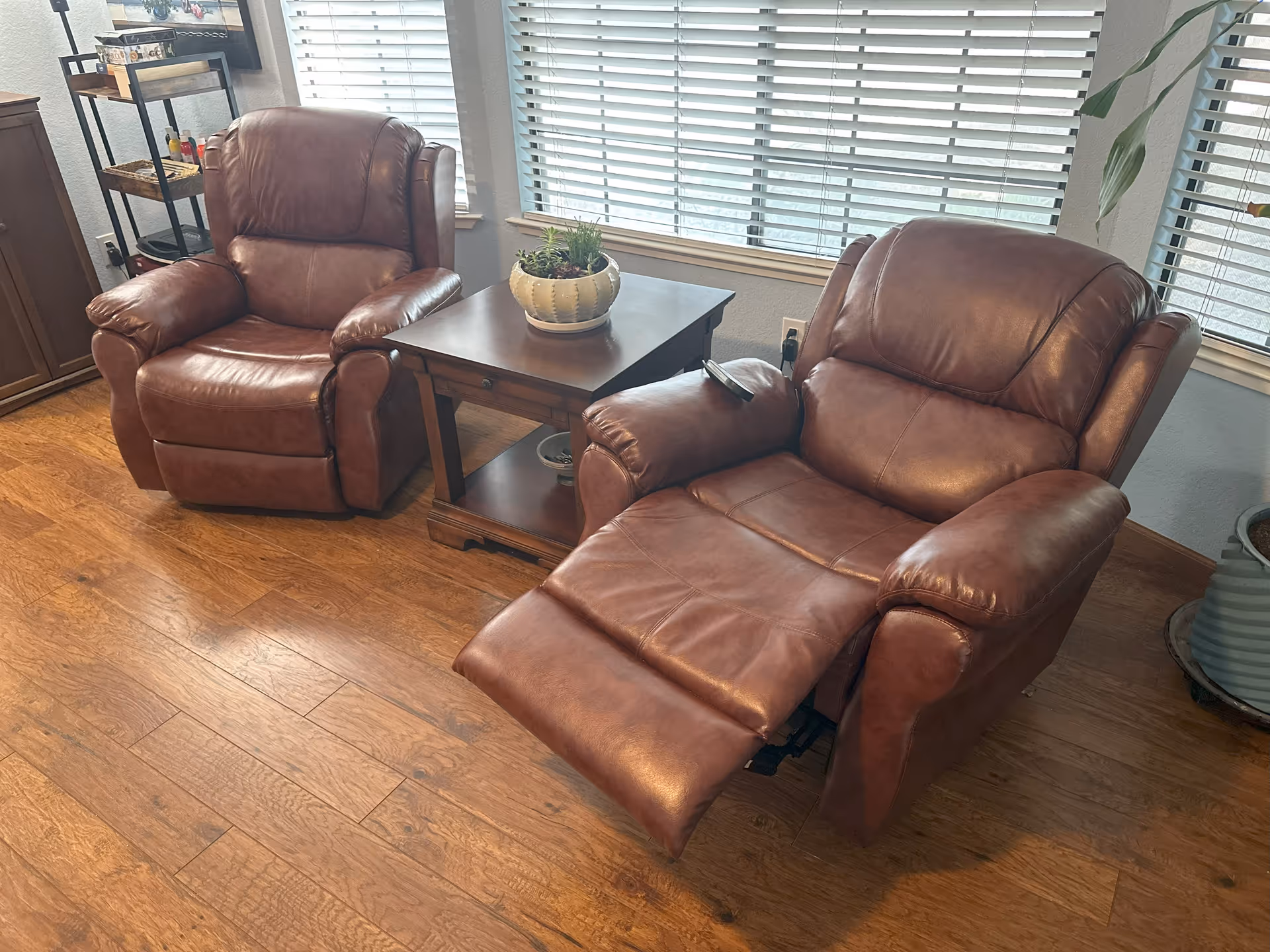 Two brown leather recliners with a side table in a sunlit living room.